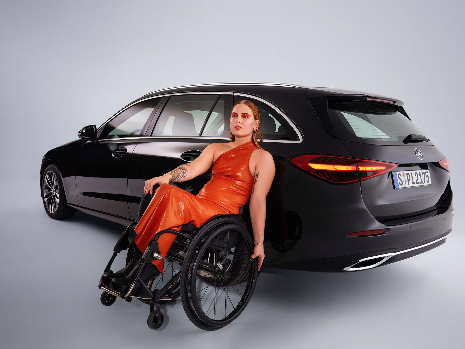 Un autovehicul adaptat persoanelor cu dizabilități - modelul Clasa C model T - într-o vedere oblică din spate și o femeie în scaun cu rotile.