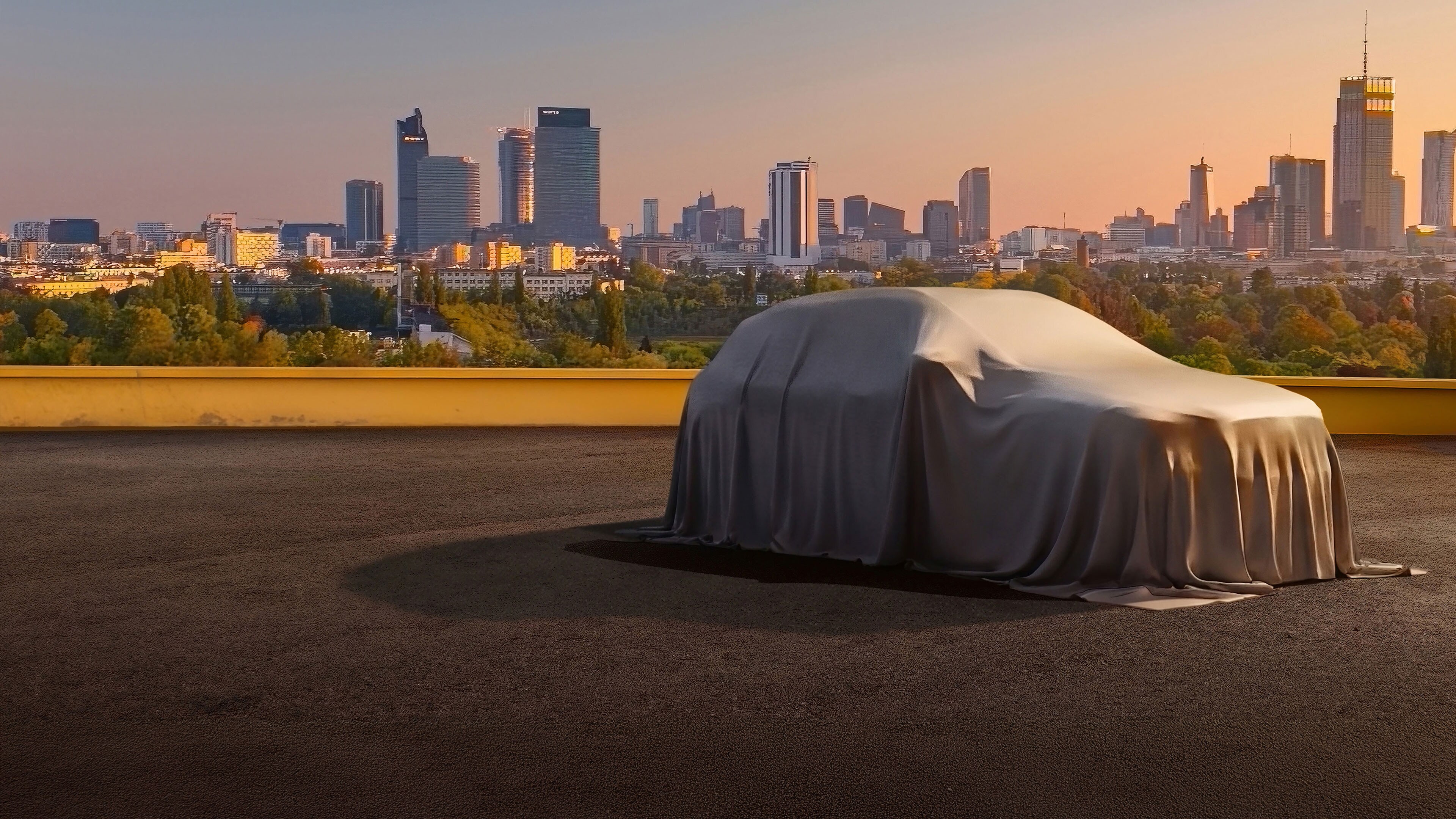 Noul Mercedes-Benz GLA voalat este prezentat dintr-o perspectivă laterală într-o parcare, pe fundalul văzându-se oraș.
