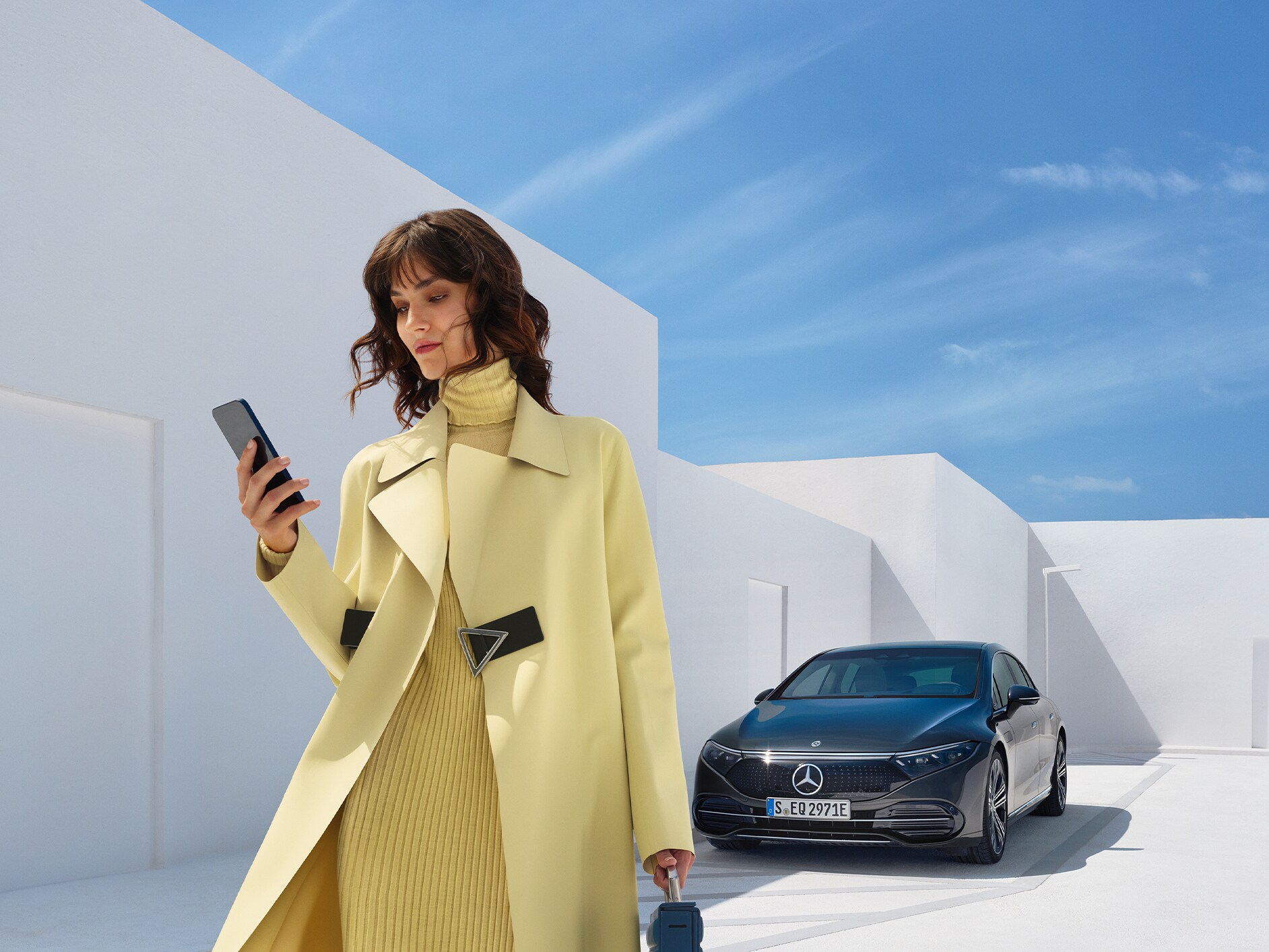 O femeie se uită la telefonul ei mobil în timp ce se îndepărtează de autovehiculul ei Mercedes-Benz electric.