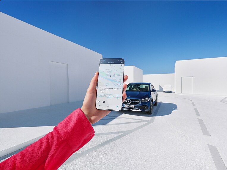 O femeie folosește aplicația Mercedes me de pe smartphone-ul său și extraopțiunile digitale pentru tema Navigație pentru a se informa cum va fi vremea la locul de destinație.