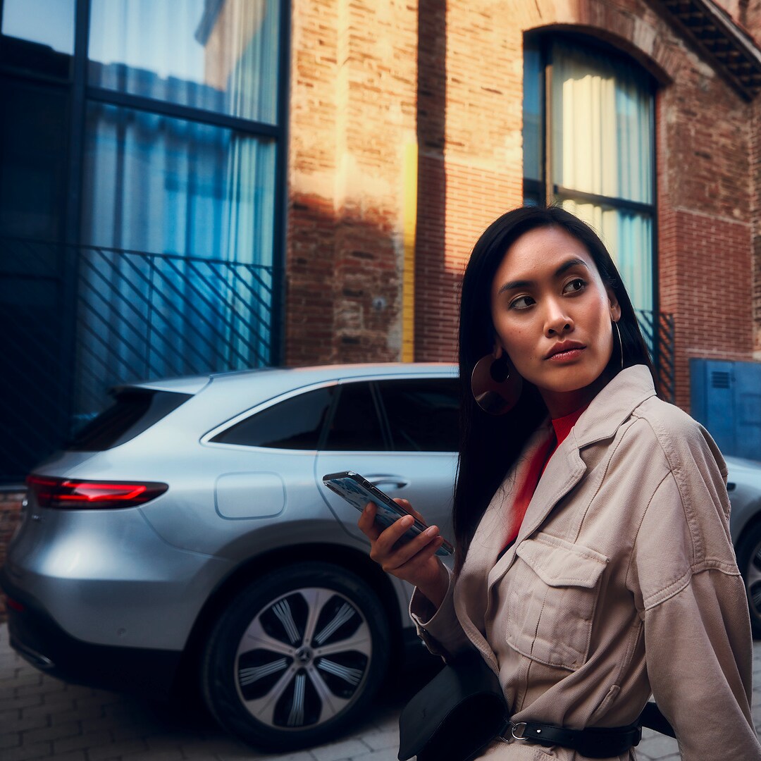 Femeie ținând un smartphone, poziționată în fața unui Mercedes-Benz