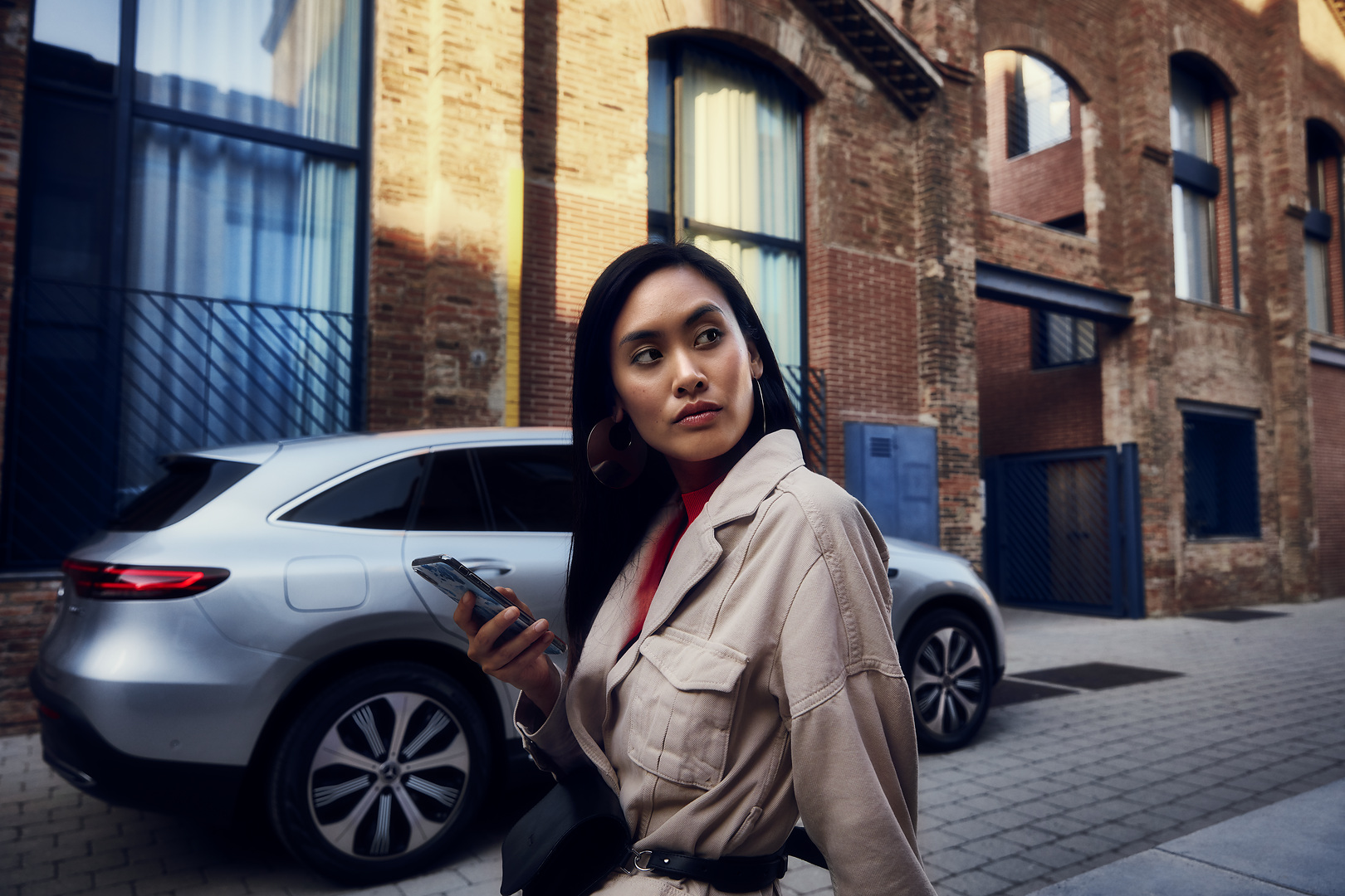 Programare vizită online | Mercedes-Benz Femeie ținând un smartphone, poziționată în fața unui Mercedes-Benz
