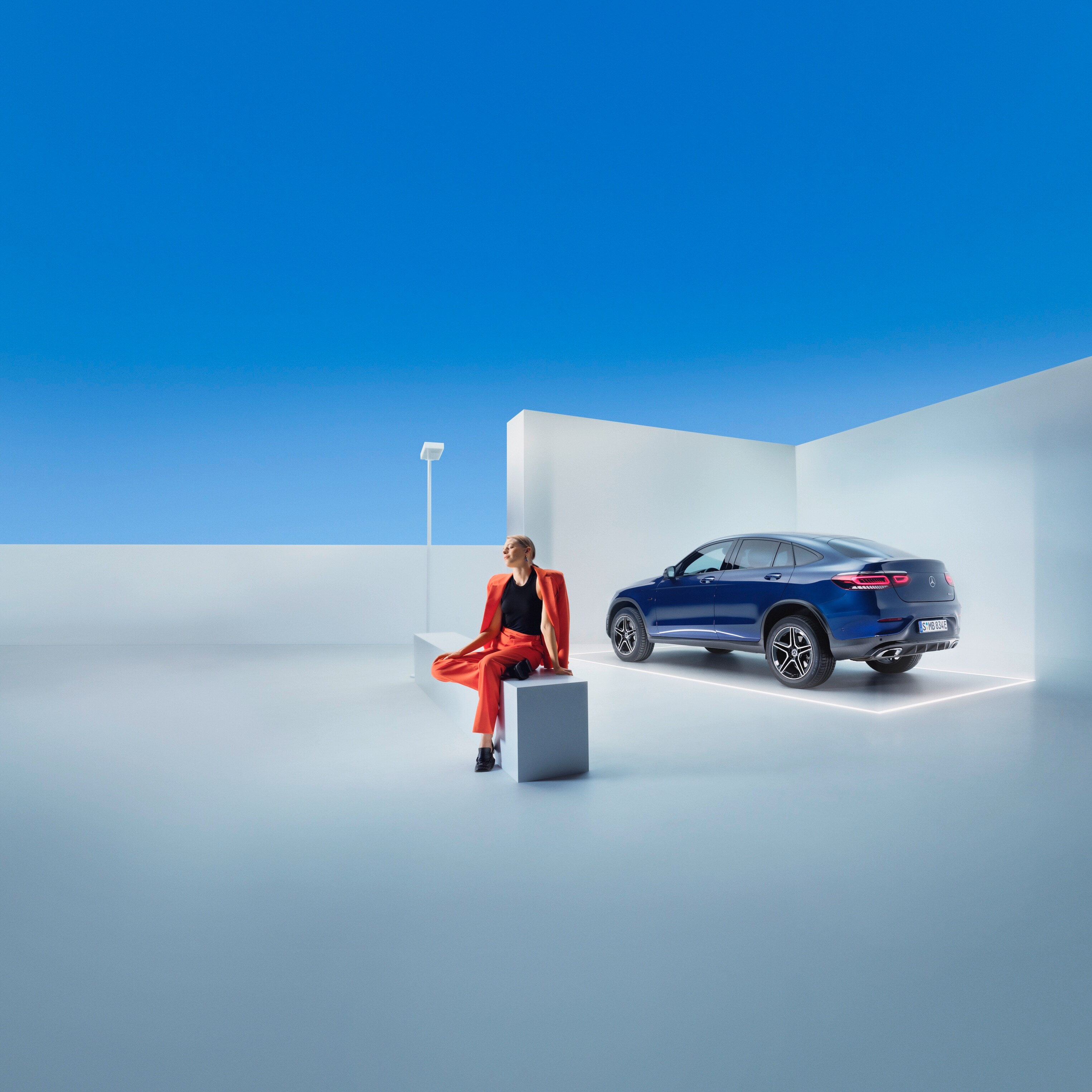 O femeie stă pe o bancă în fața unui Mercedes-Benz.