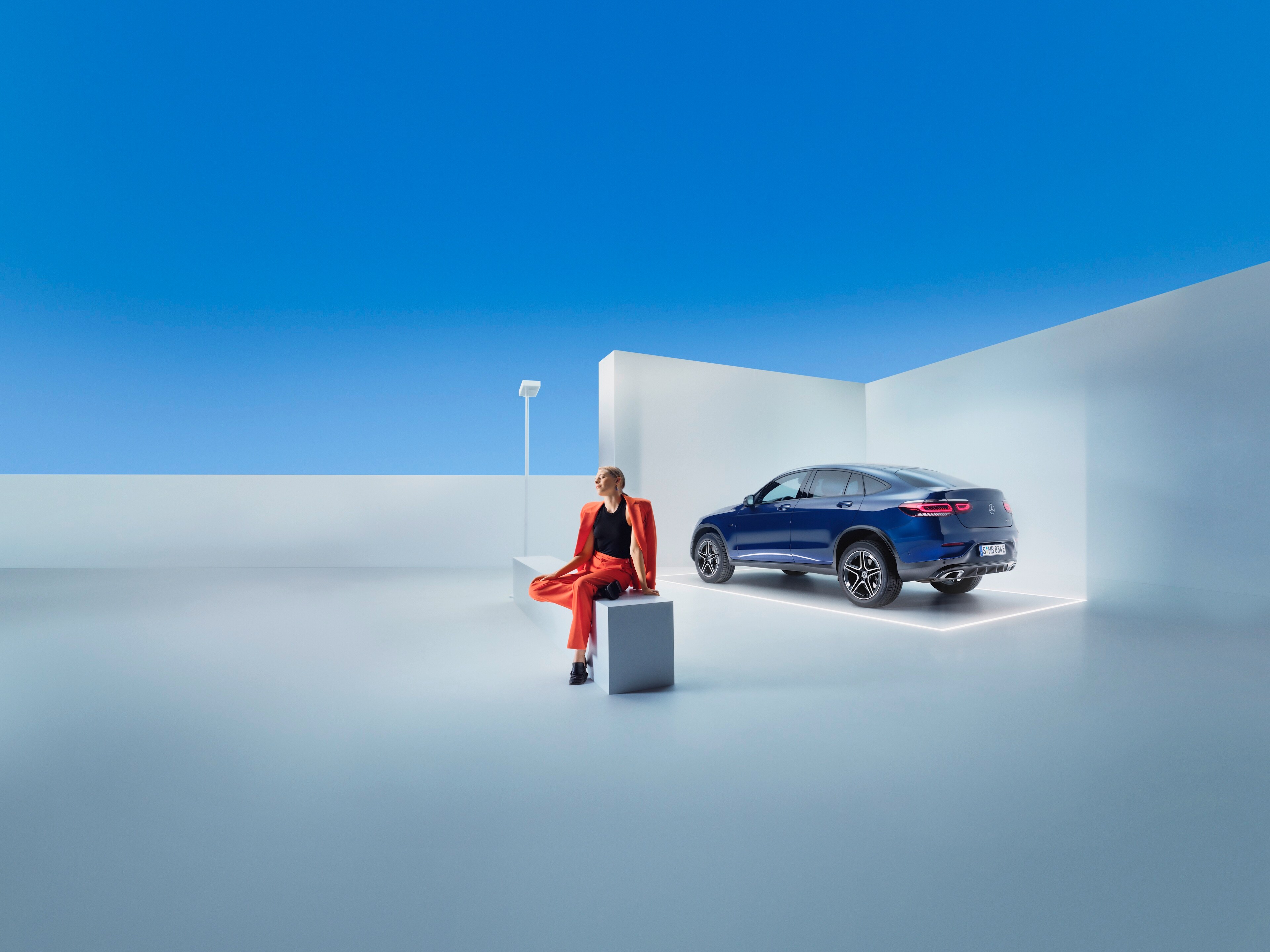 O femeie se relaxează pe o bancă în fața autovehiculului său Mercedes-Benz.