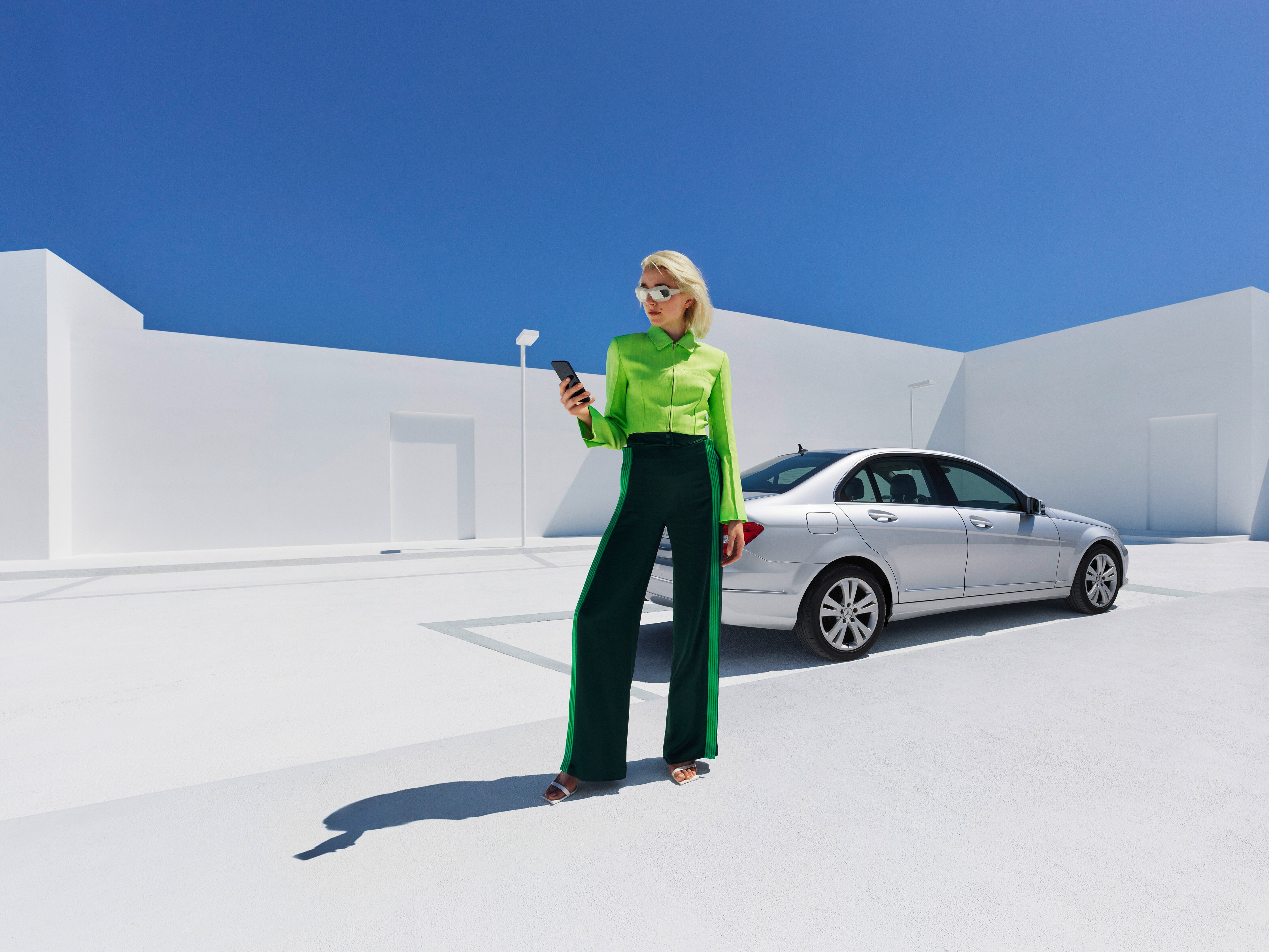O femeie își verifică telefonul în timp ce stă în fața autovehiculului ei Mercedes-Benz.