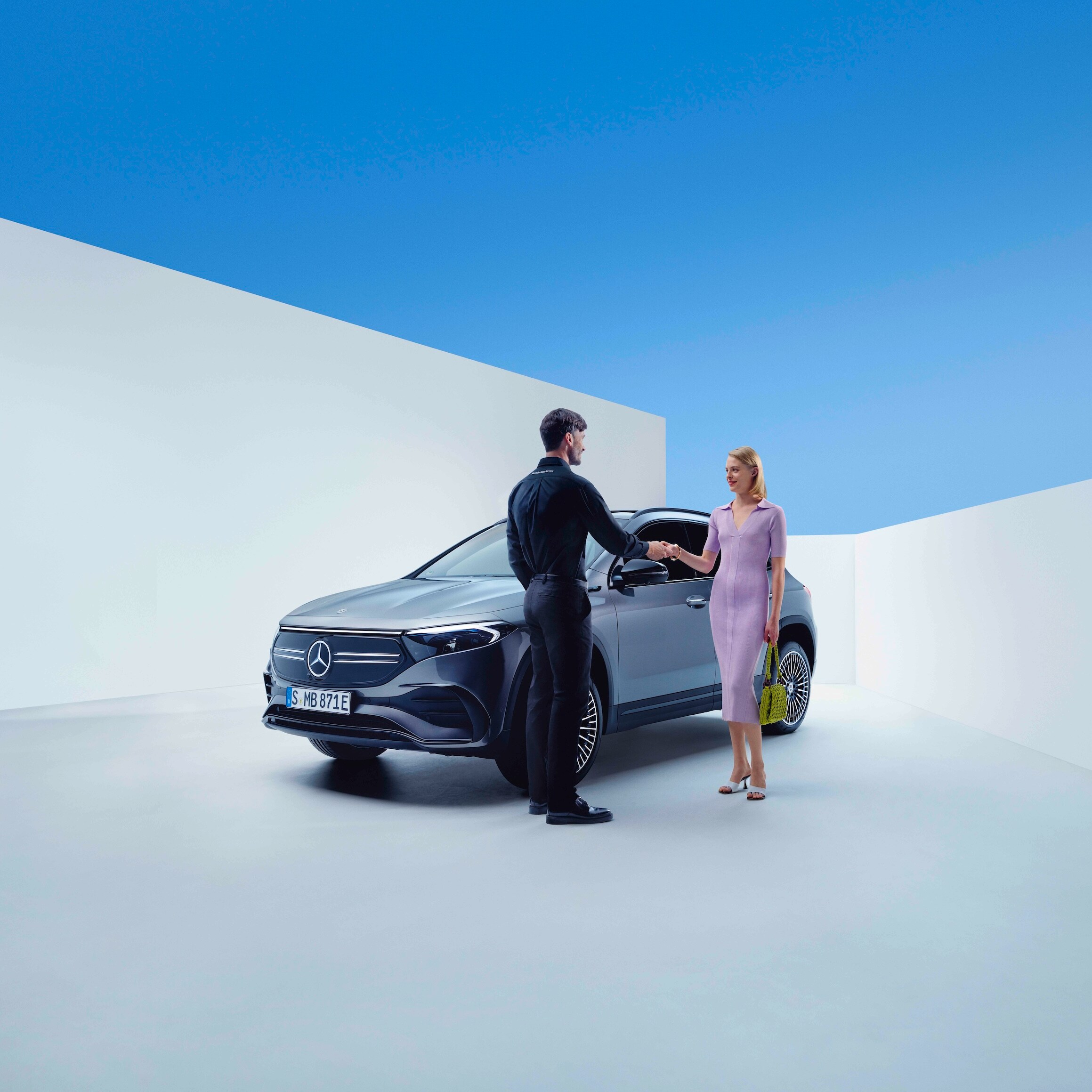 Un angajat Mercedes-Benz și o femeie își dau mâna în fața unui Mercedes-Benz