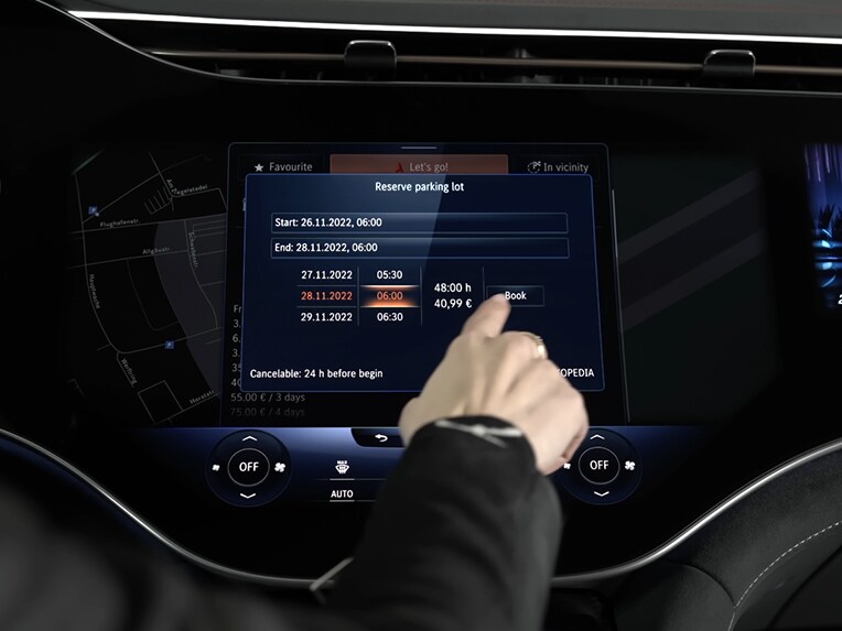 O persoană apasă pe afișajul autovehiculului și folosește Off-Street Booking pentru a rezerva un spațiu de parcare disponibil prin intermediul sistemului MBUX.