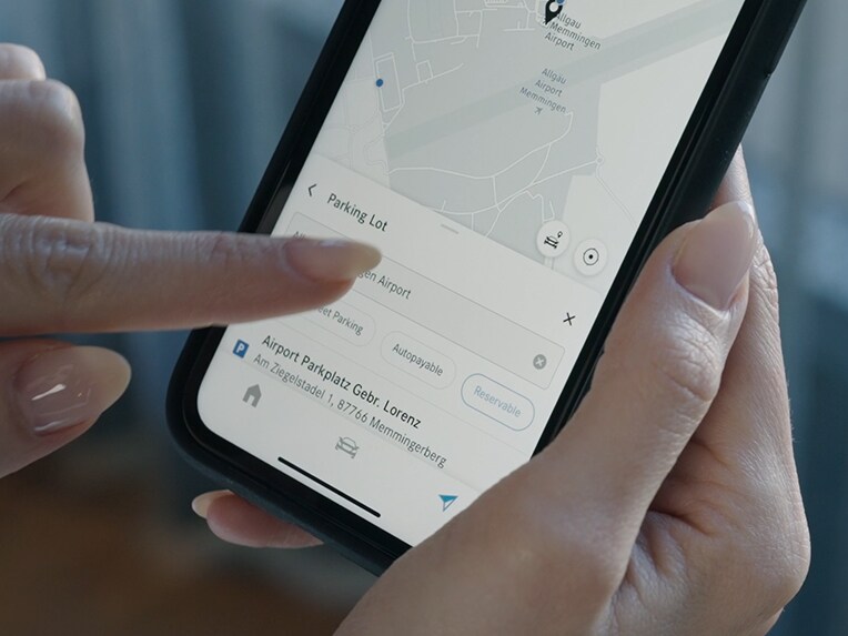 O persoană apasă pe ecranul smartphone-ului și folosește Off-Street Parking pentru a afișa prețurile spațiilor de parcare disponibile.
