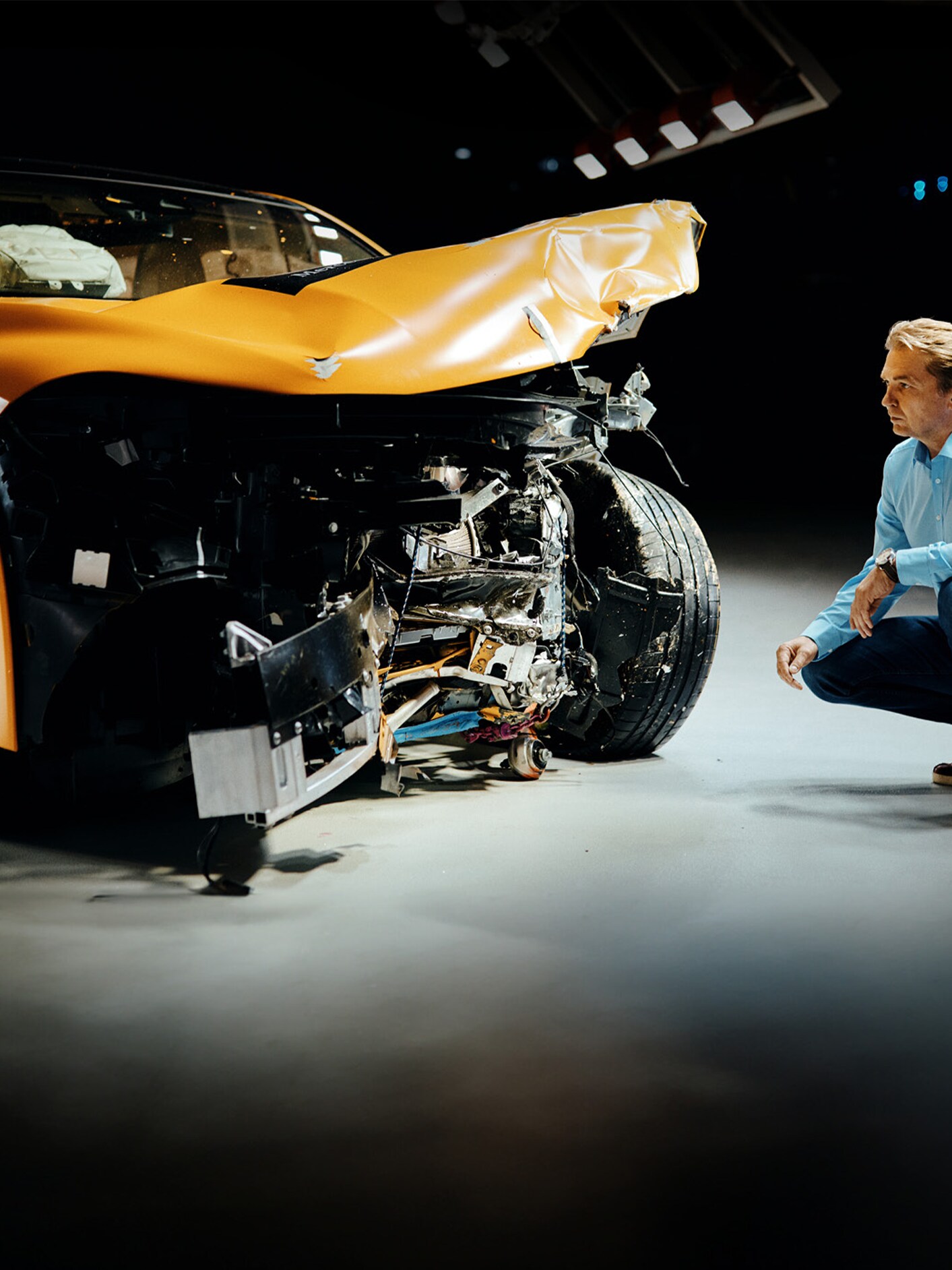 Un expert în testele de impact examinează un autovehicul Mercedes-Benz lovit frontal, în timp ce stă ghemuit lângă ea.