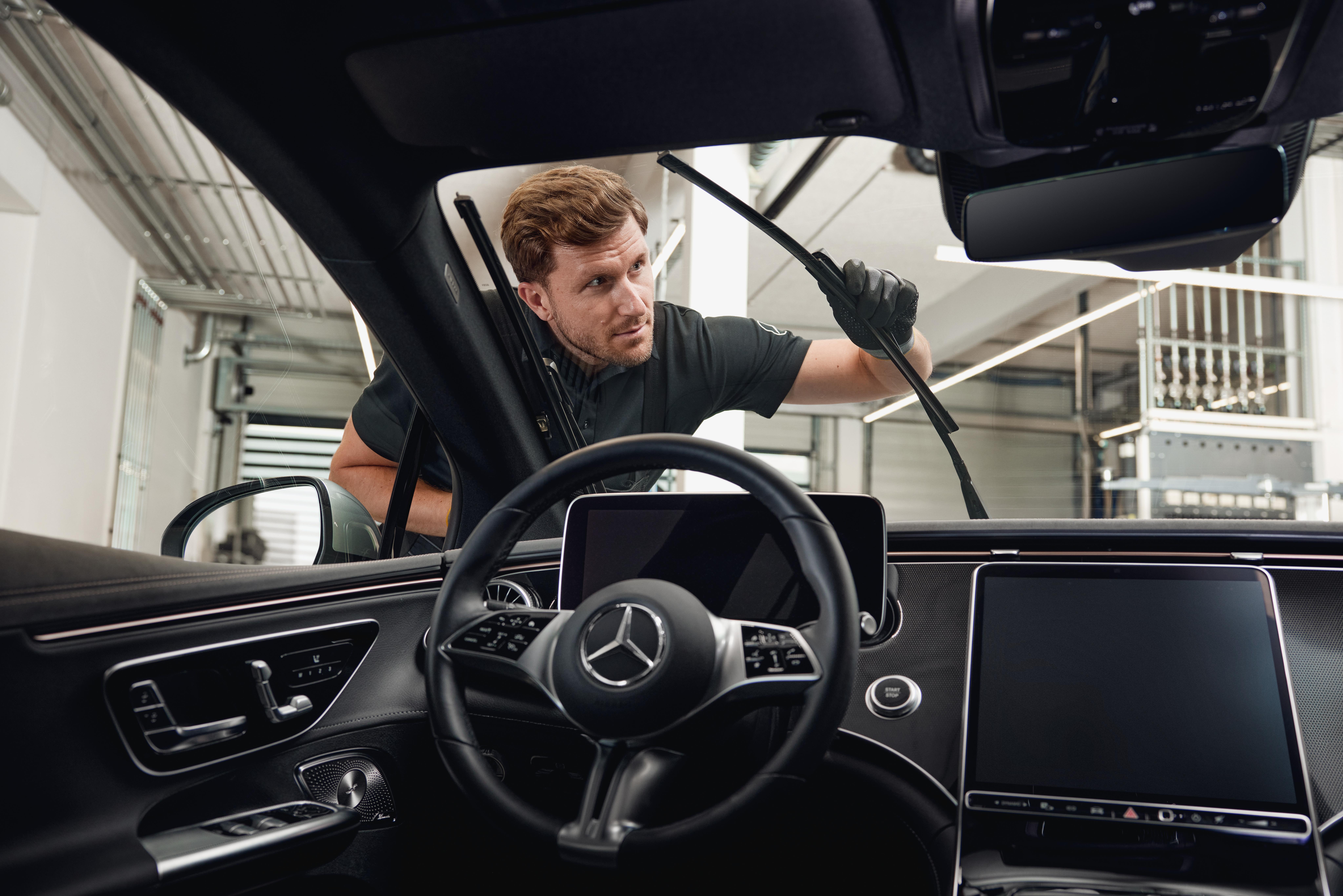 Lamele pentru ștergătoare de origine Mercedes-Benz Vedere din interiorul unui autovehicul Mercedes-Benz cu un tehnician care înlocuiește lamele de origine ale ștergătoarelor.