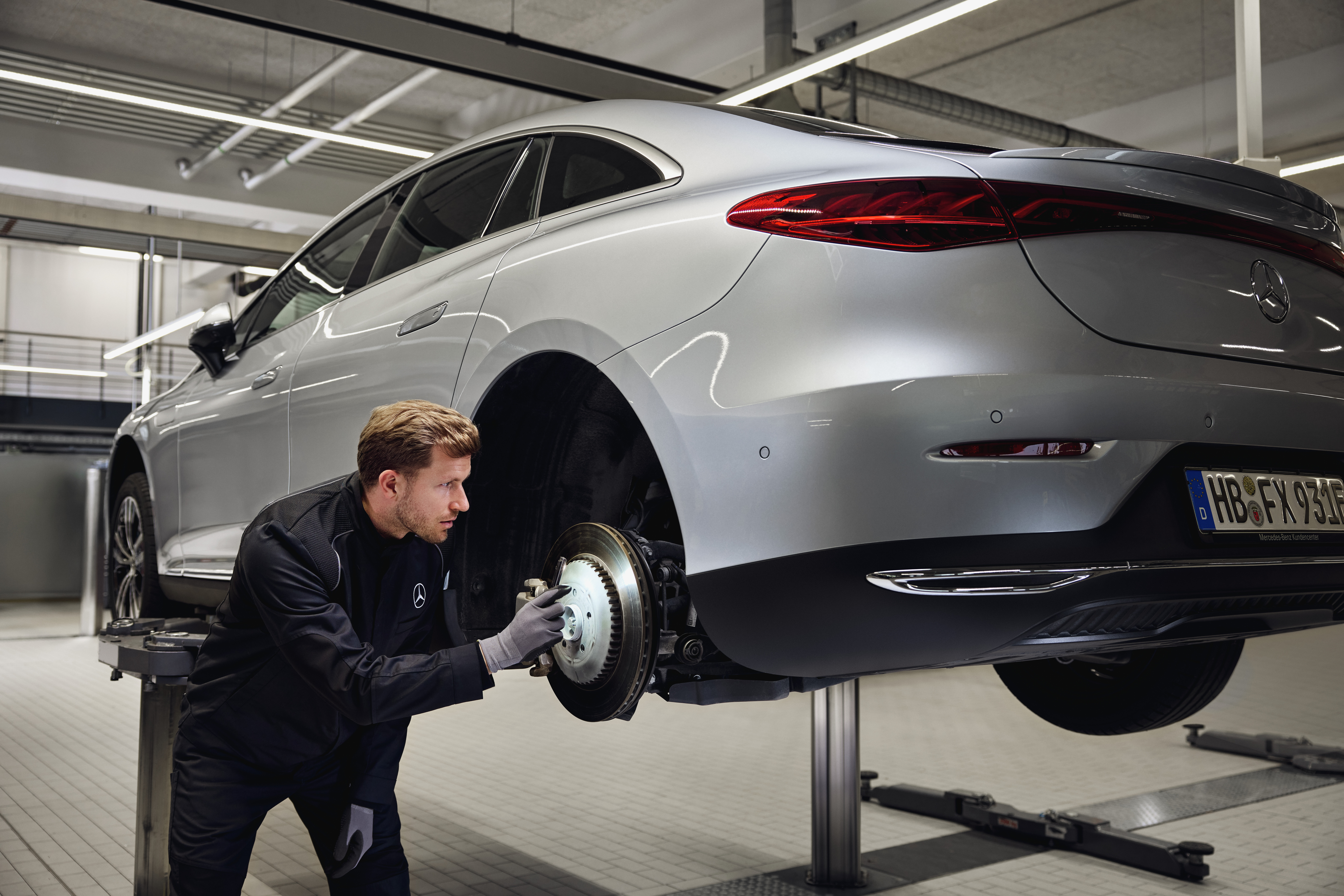 Înlocuirea frânelor de origine Mercedes-Benz Un autovehicul Mercedes-Benz ridicat pe un elevator, cu un tehnician care inspectează sistemul de frânare.