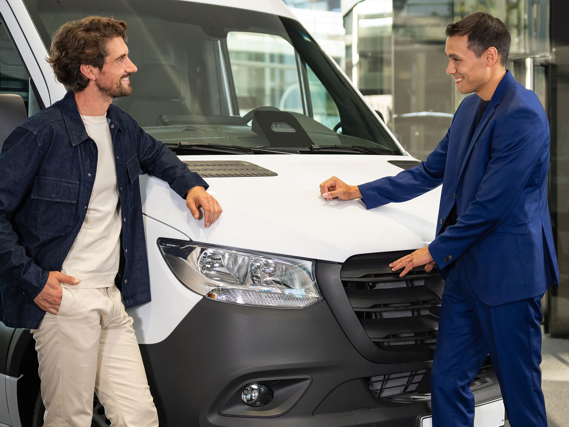 Două persoane sprijinite de o furgonetă Mercedes-Benz și purtând o conversație.