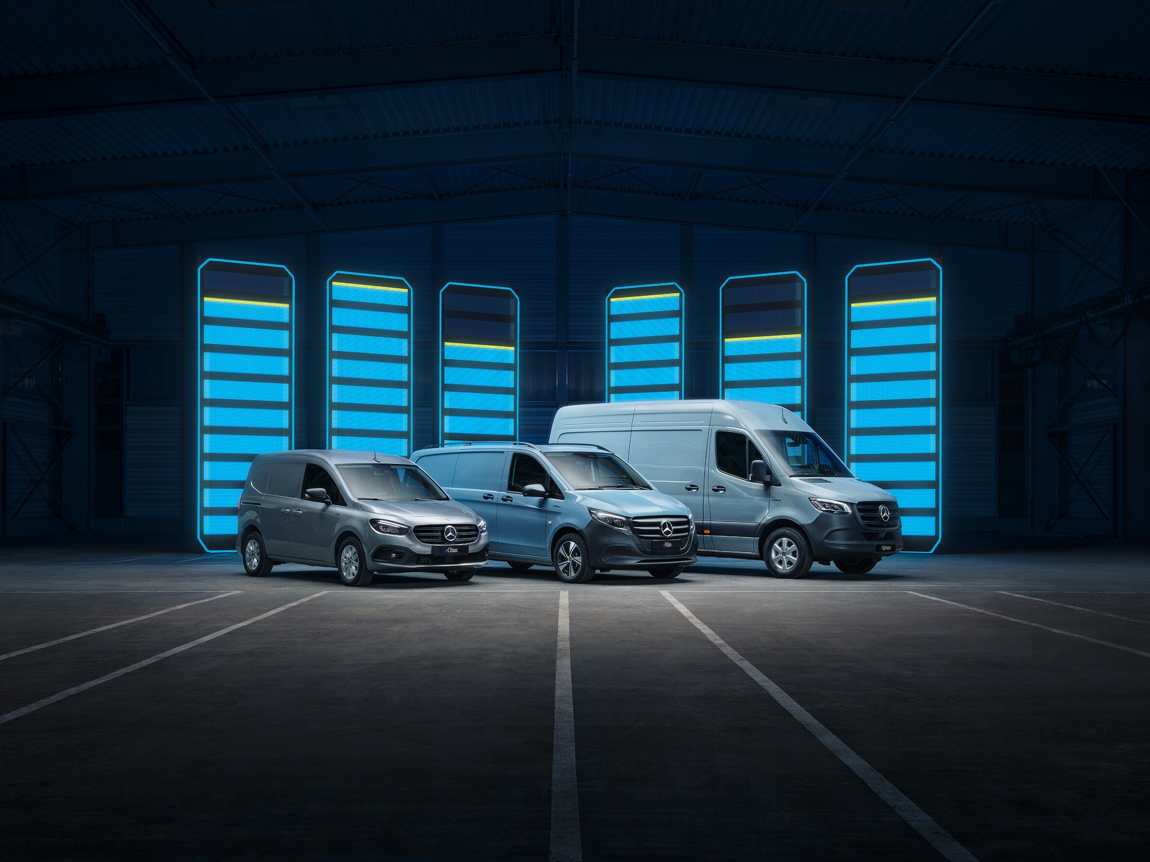 Gama de autovehicule comerciale electrice Mercedes-Benz prezentate într-un depozit futurist, cu bare de încărcare iluminate