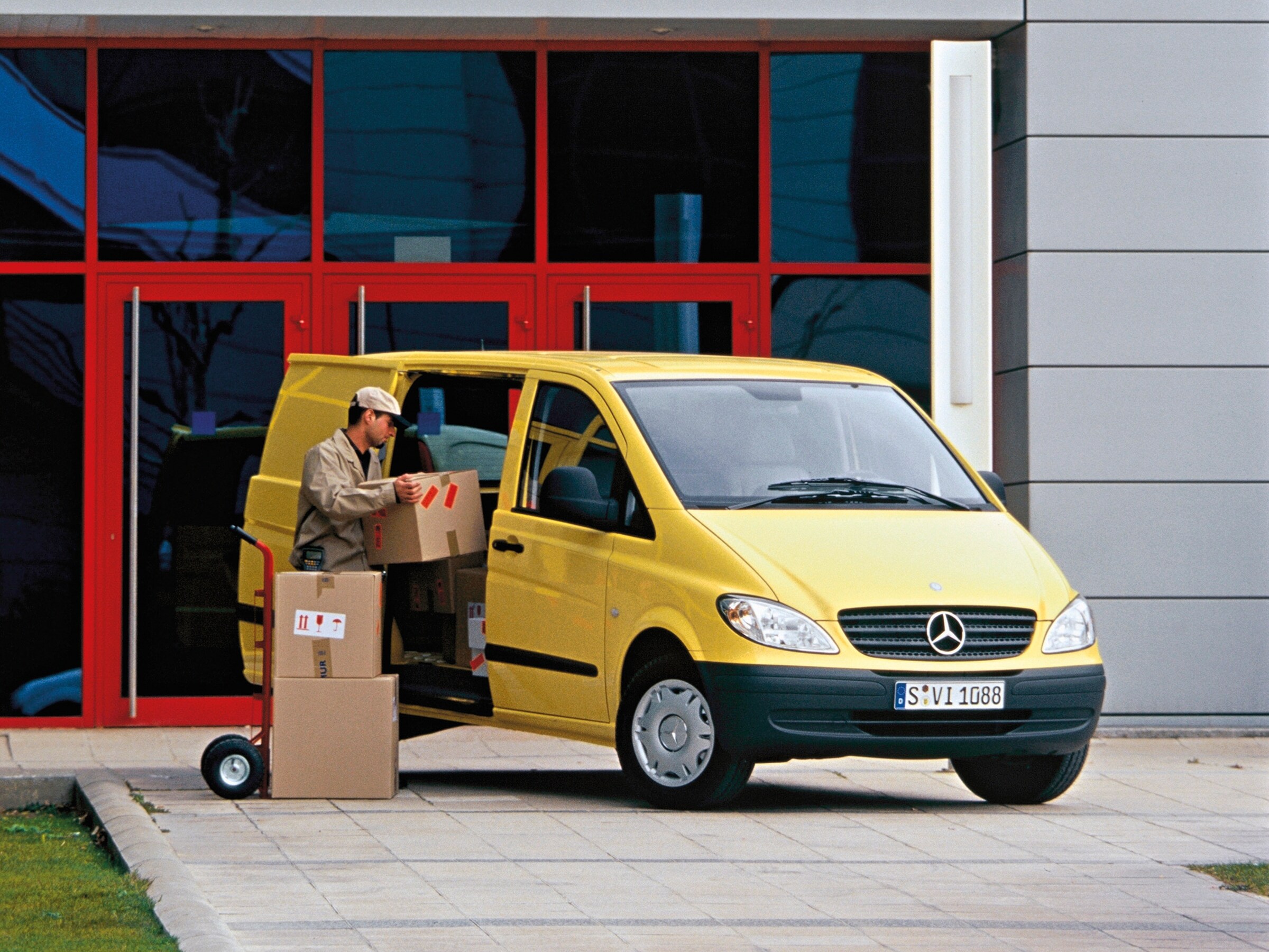 Un Vito galben de la Mercedes-Benz Vito, parcat în afara clădirii, cu angajați descărcând bagaje