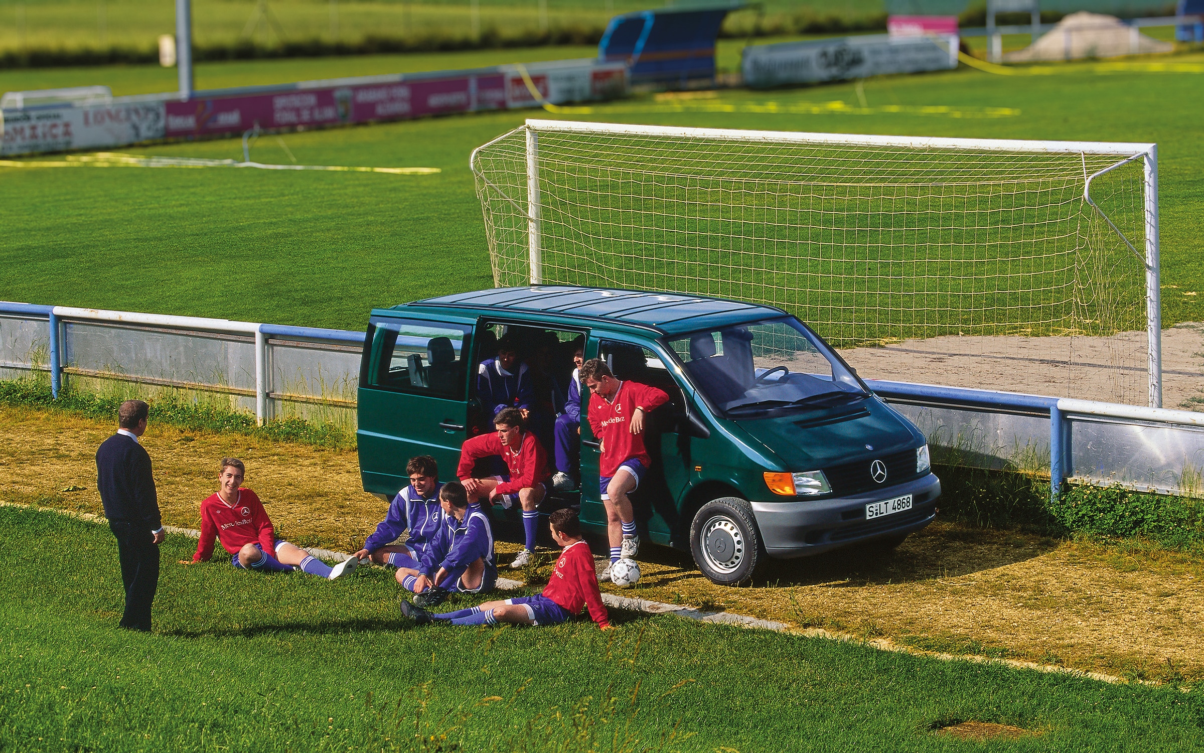 Prima generație de modele Vito de la Mercedes-Benz | Istoria autovehiculelor utilitare | Mercedes-Benz Vito din prima generație parcat lângă un teren de fotbal, cu echipe de jucători în apropiere