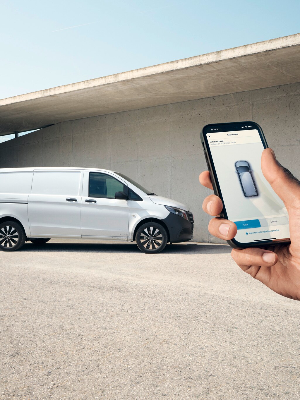 Smartphone cu aplicația Mercedes-Benz afișată. eVito furgon în fundal.