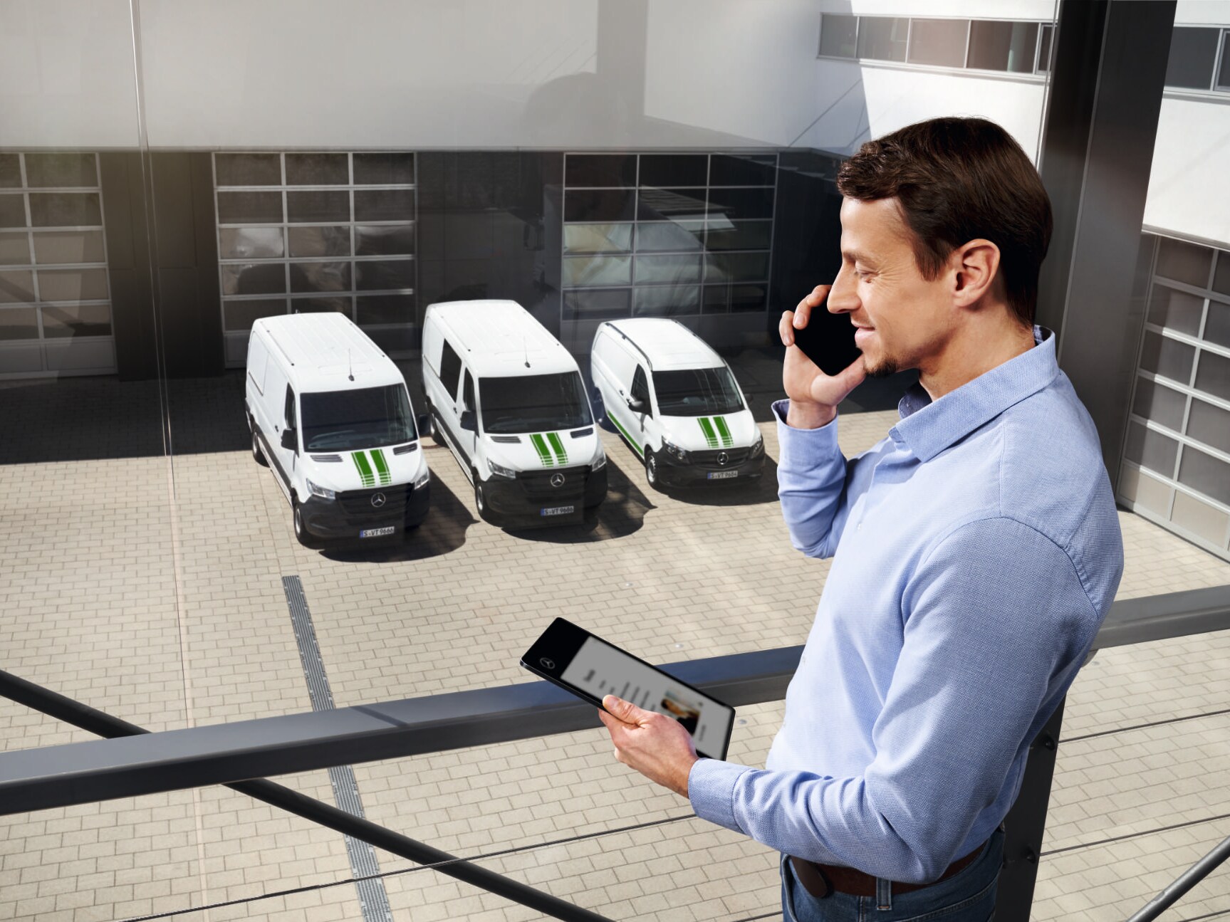 Un consultant Mercedes-Benz, cu un telefon și o tabletă, autovehicule Mercedes-Benz în fundal.