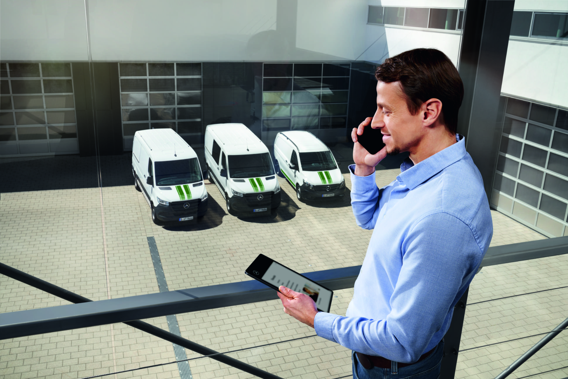 Van Uptime Monitor | Extraopțiuni Digitale | Mercedes-Benz Un consultant Mercedes-Benz, cu un telefon și o tabletă, autovehicule Mercedes-Benz în fundal.