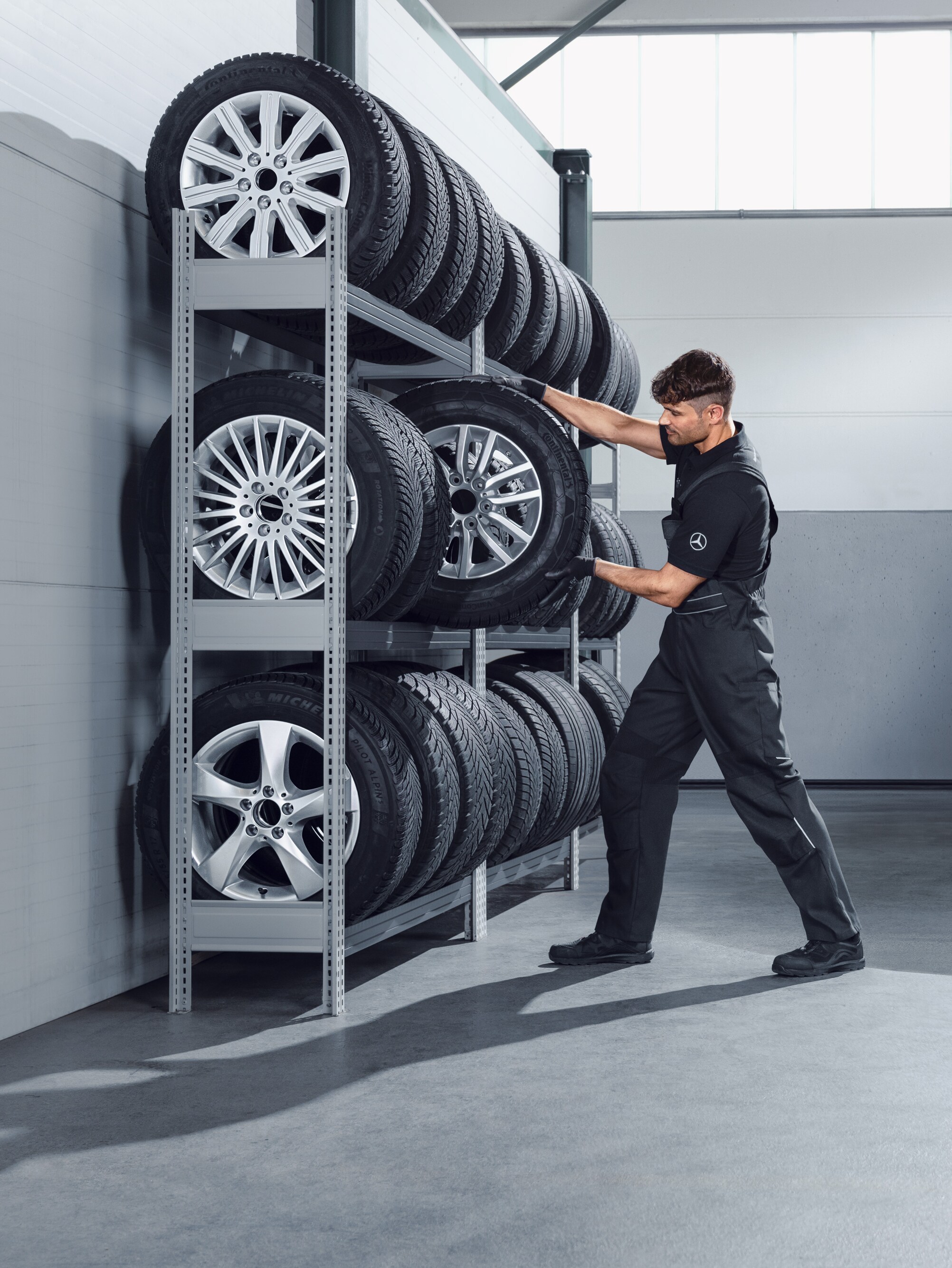 Mecanic selectând roți complete de iarnă Mercedes-Benz pentru un model Sprinter alb de pe raftul atelierului.