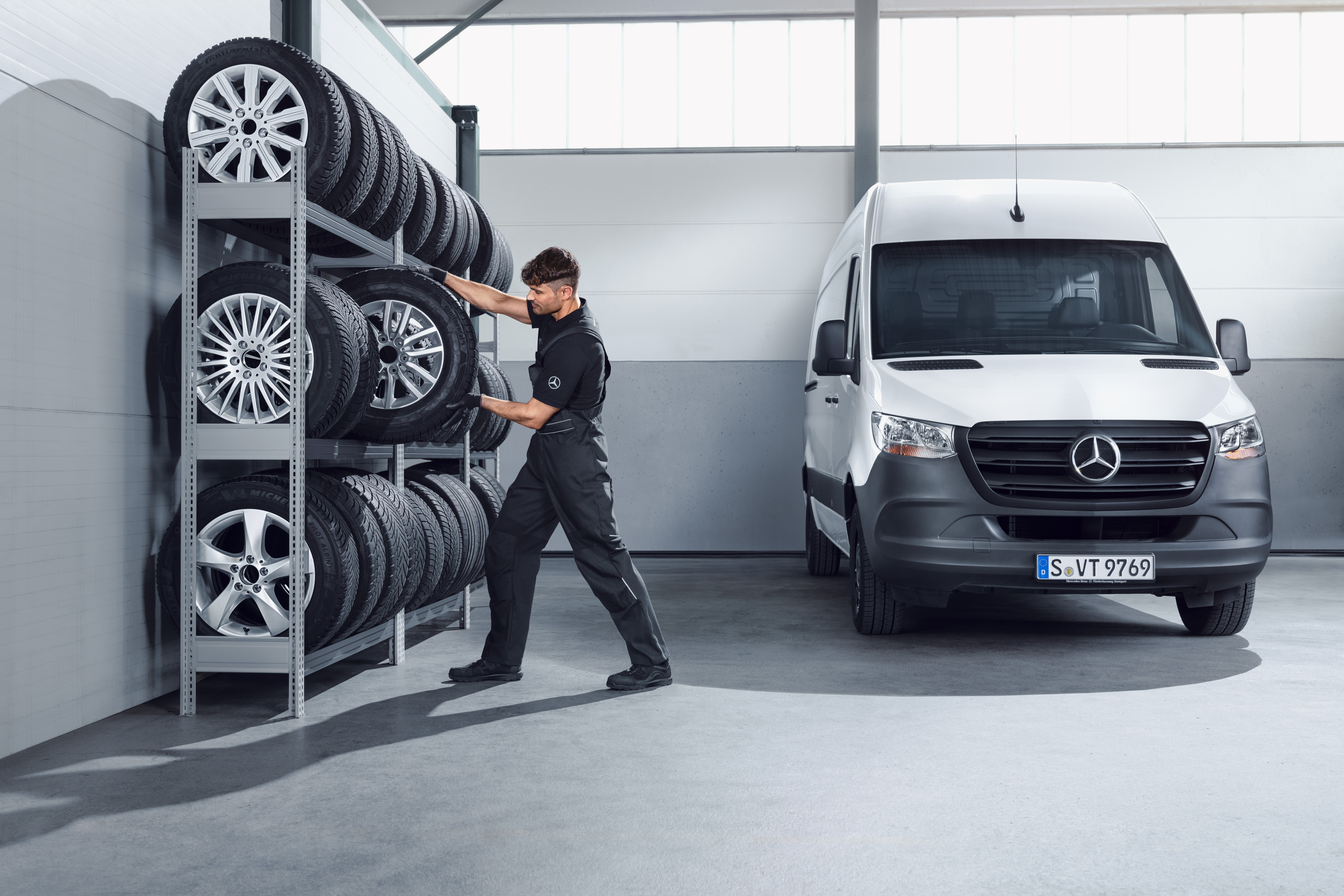 Mercedes-Benz | Piese de origine de calitate pentru autovehicule comerciale Mecanic selectând roți complete de iarnă Mercedes-Benz pentru un model Sprinter alb de pe raftul atelierului.