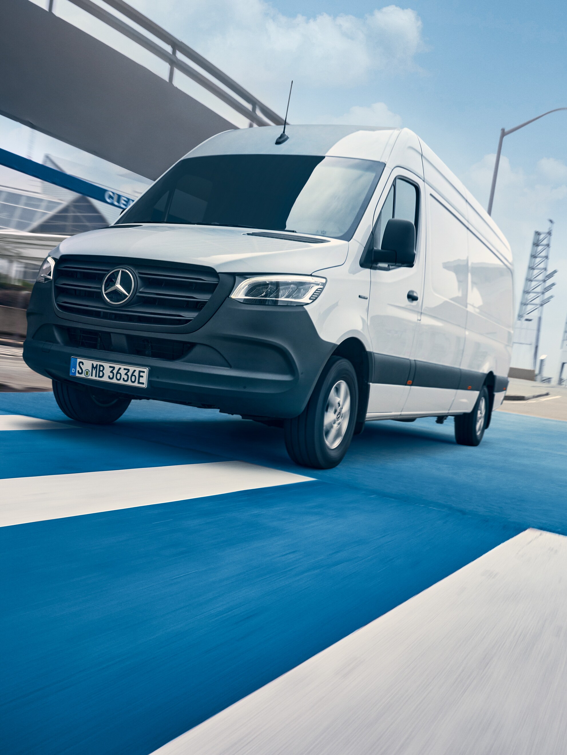 O furgonetă Mercedes-Benz Sprinter albă circulă pe un drum dintr-un oraș.