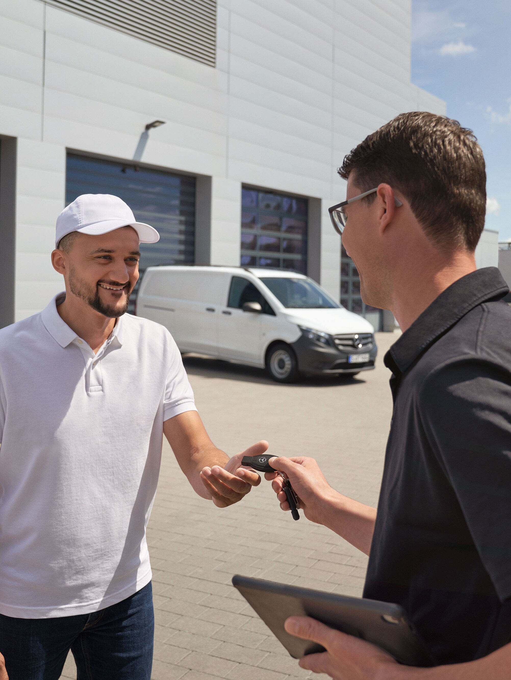 Un tehnician înmânează telecomanda unui client cu o furgonetă Mercedes-Benz Vito albă în fundal.