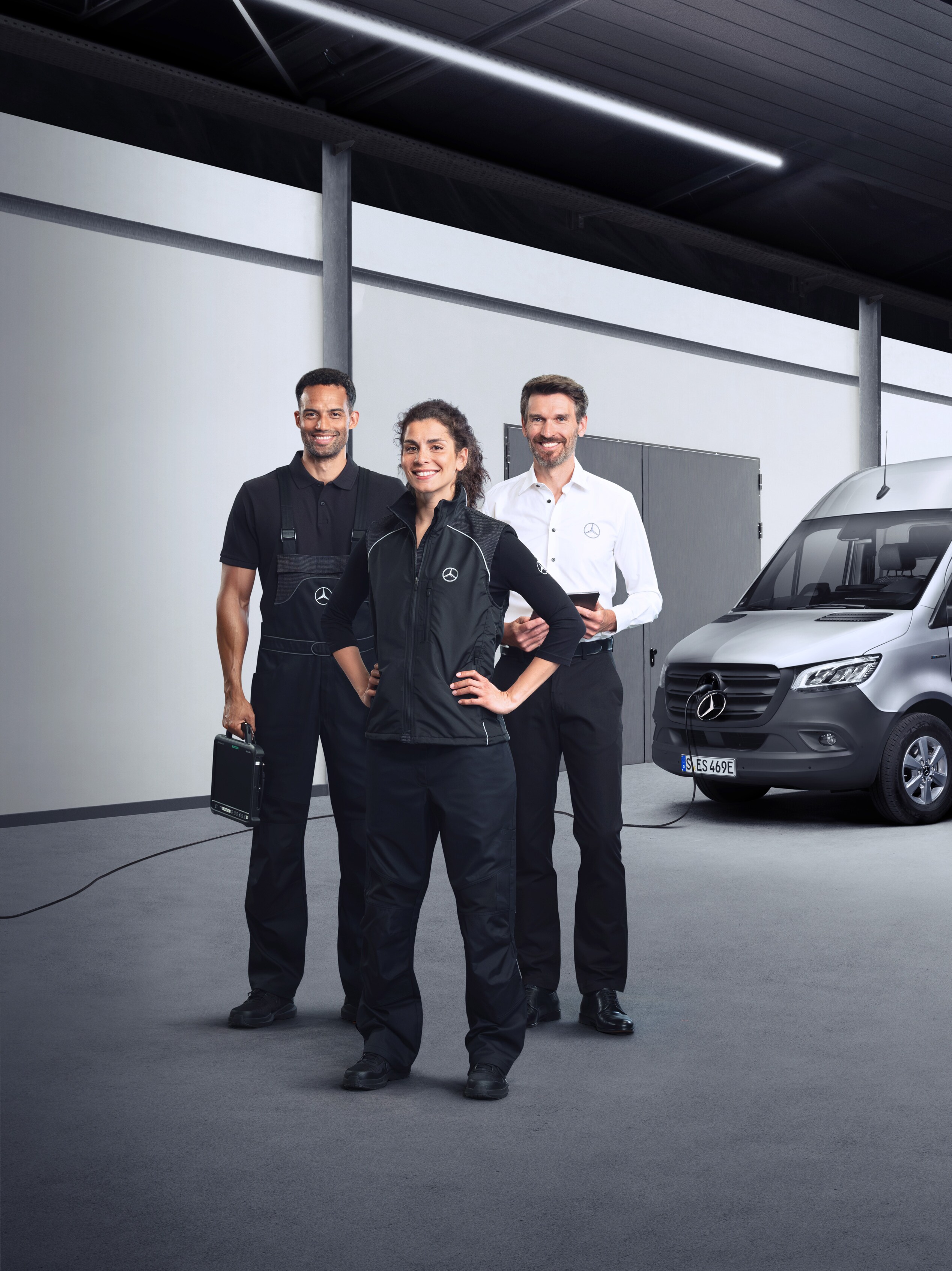Trei angajați în fața unui Mercedes-Benz eSprinter, cu cablu de încărcare conectat.