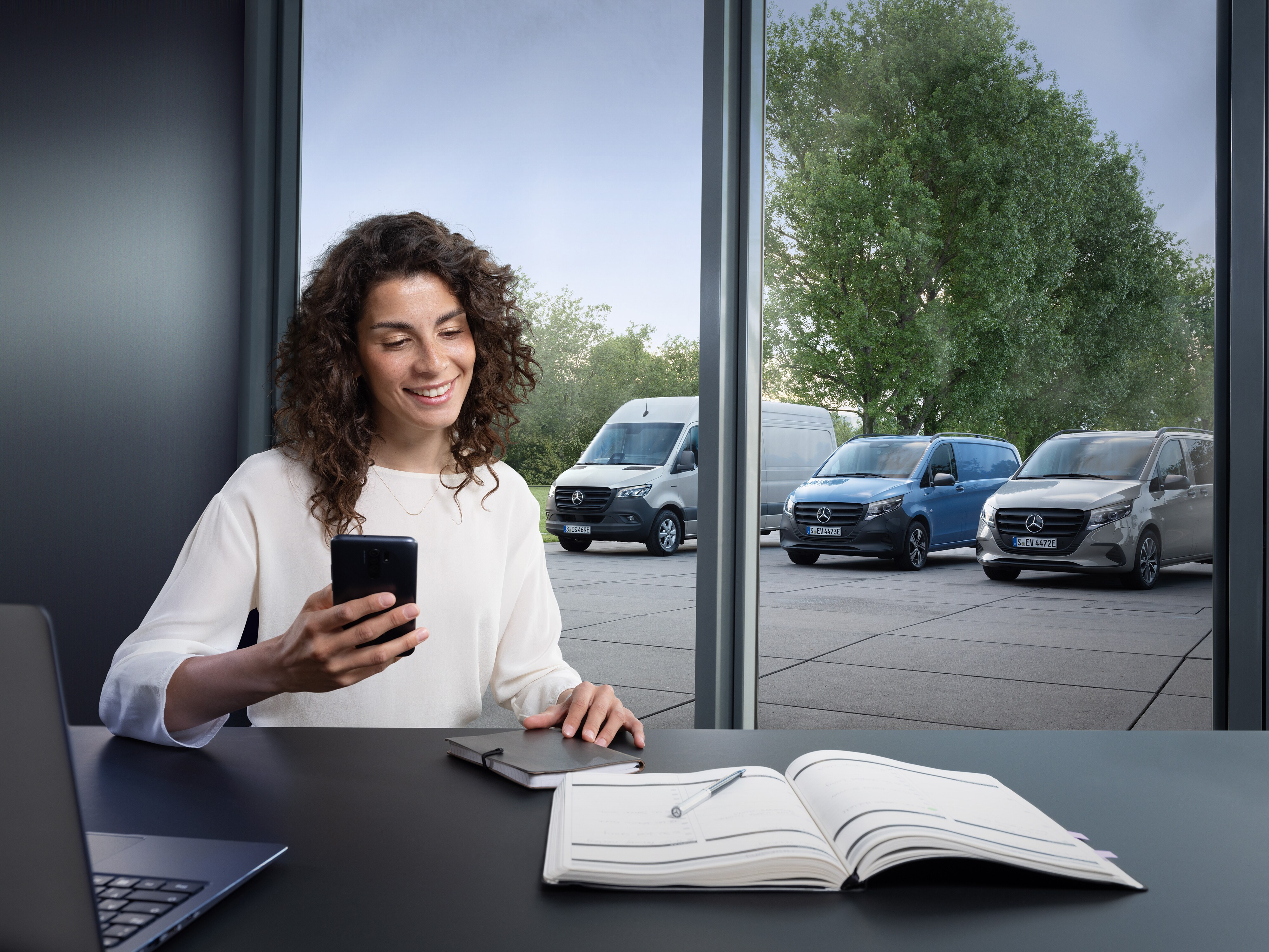 O femeie face planuri pe smartphone în fața unei furgonete Mercedes-Benz